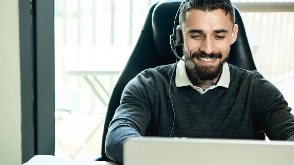 Smiling support agent with a headset working at a laptop